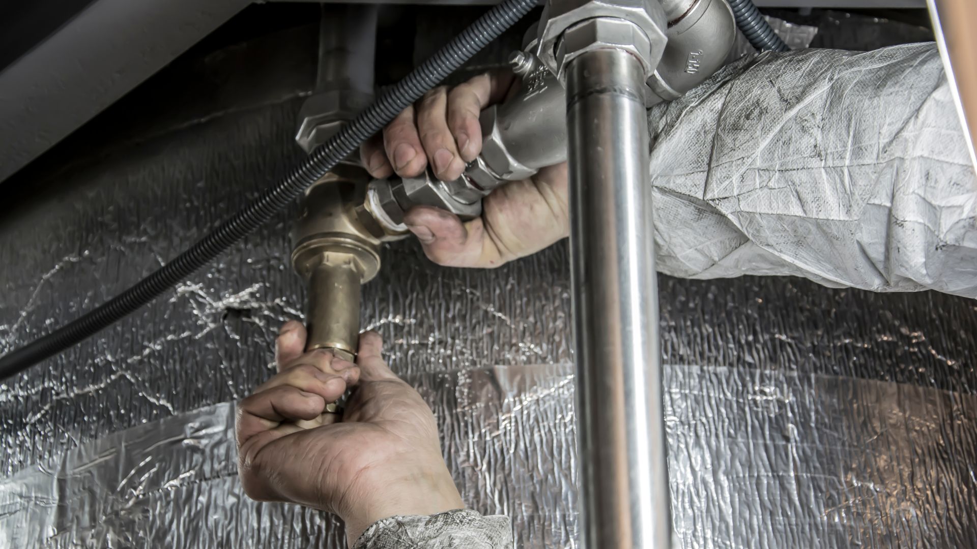 Hands tightening plumbing pipe connections with wrench in industrial setting