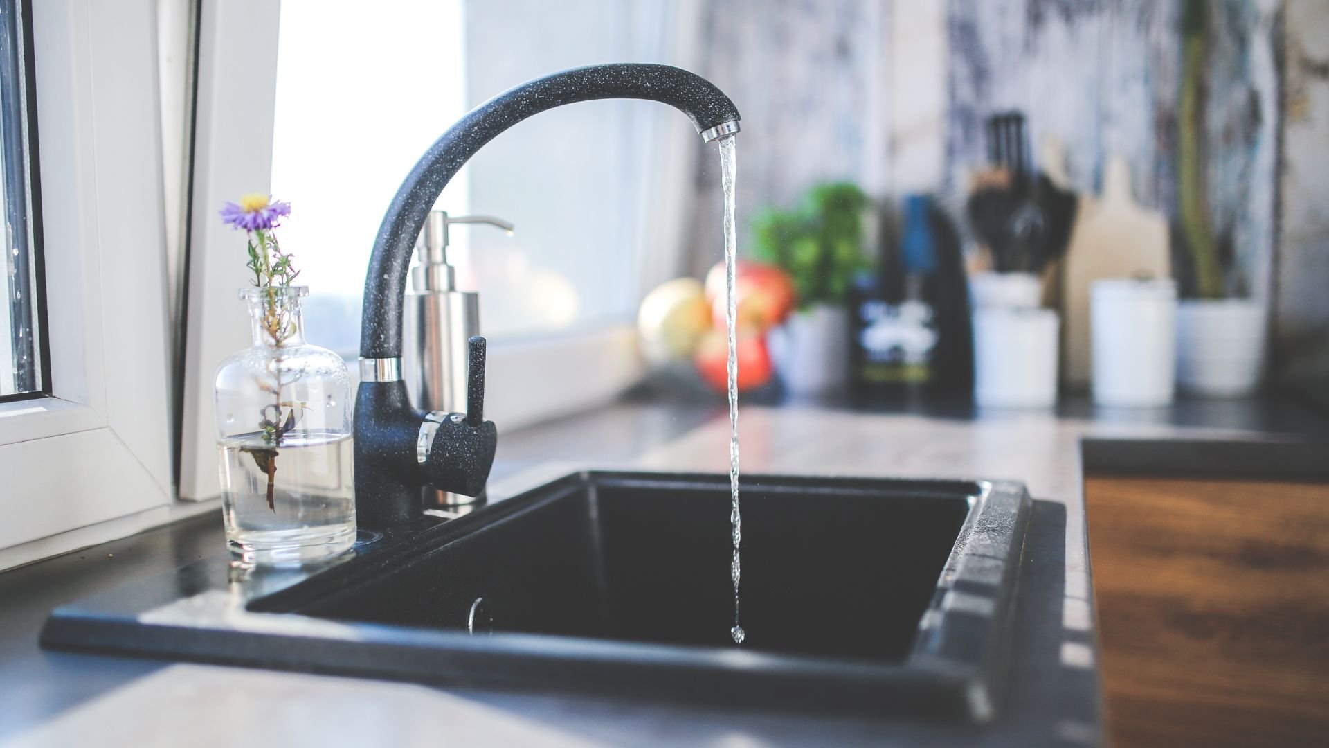 Running water from black faucet into dark sink with flower in glass jar
