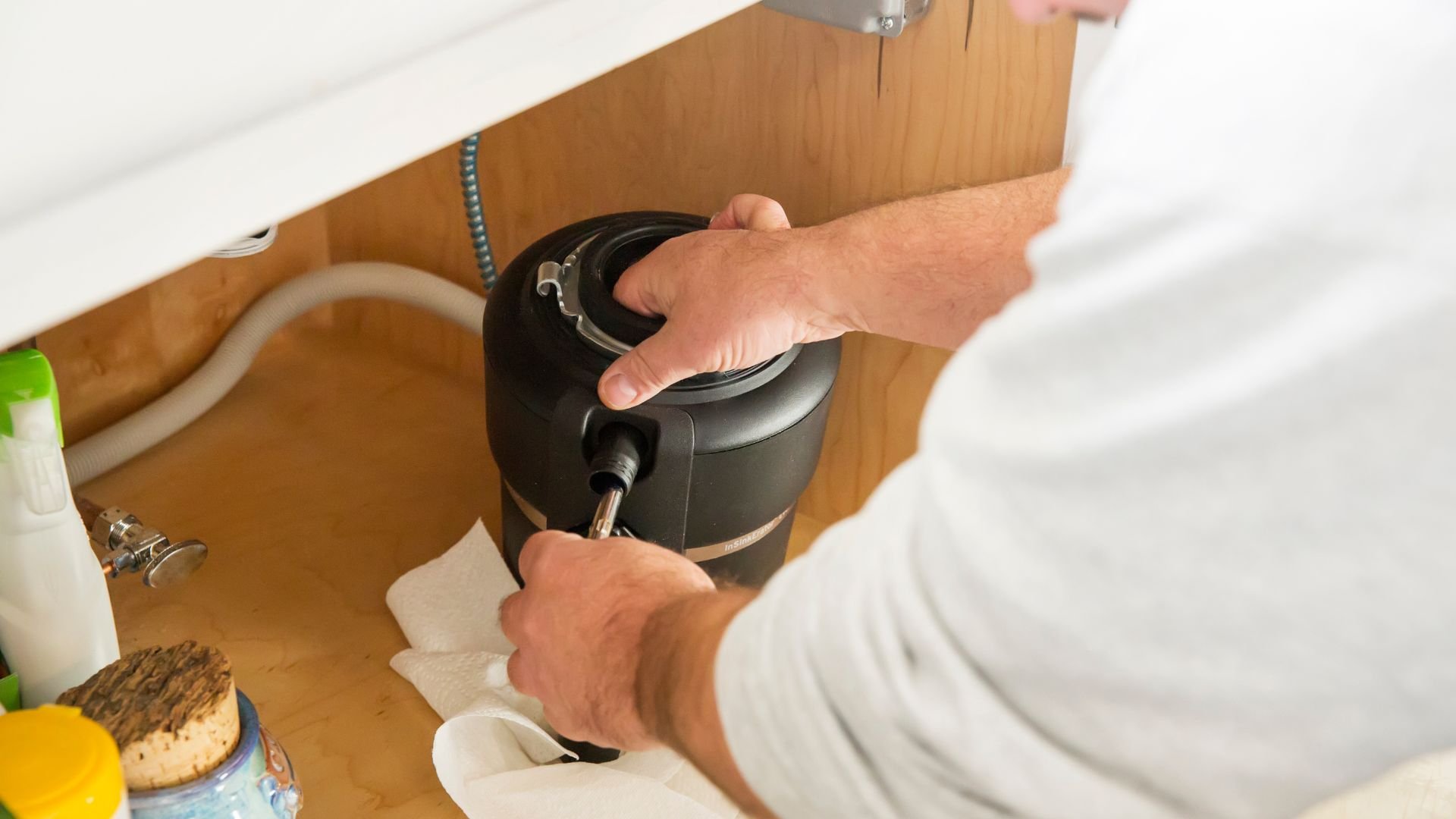 Hands operating a garbage disposal under a kitchen sink