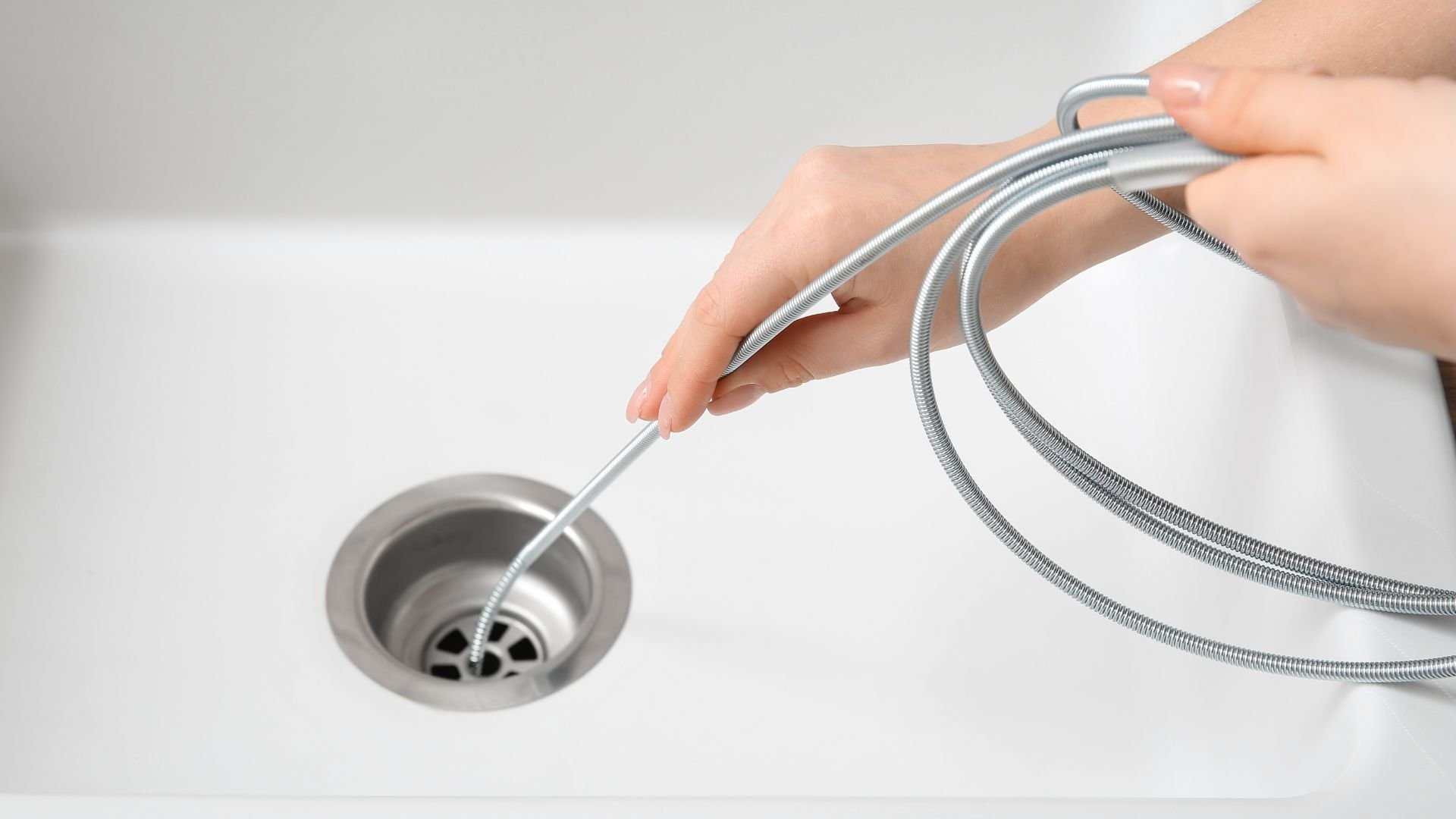 Hand inserting flexible drain snake into sink drain
