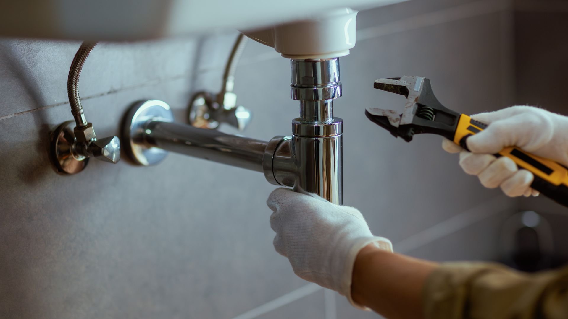 Plumber fixing sink pipe with wrench and gloved hands